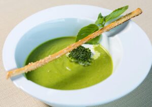A bright green pea soup in a white bowl, garnished with croutons and herbs, elegantly presented.